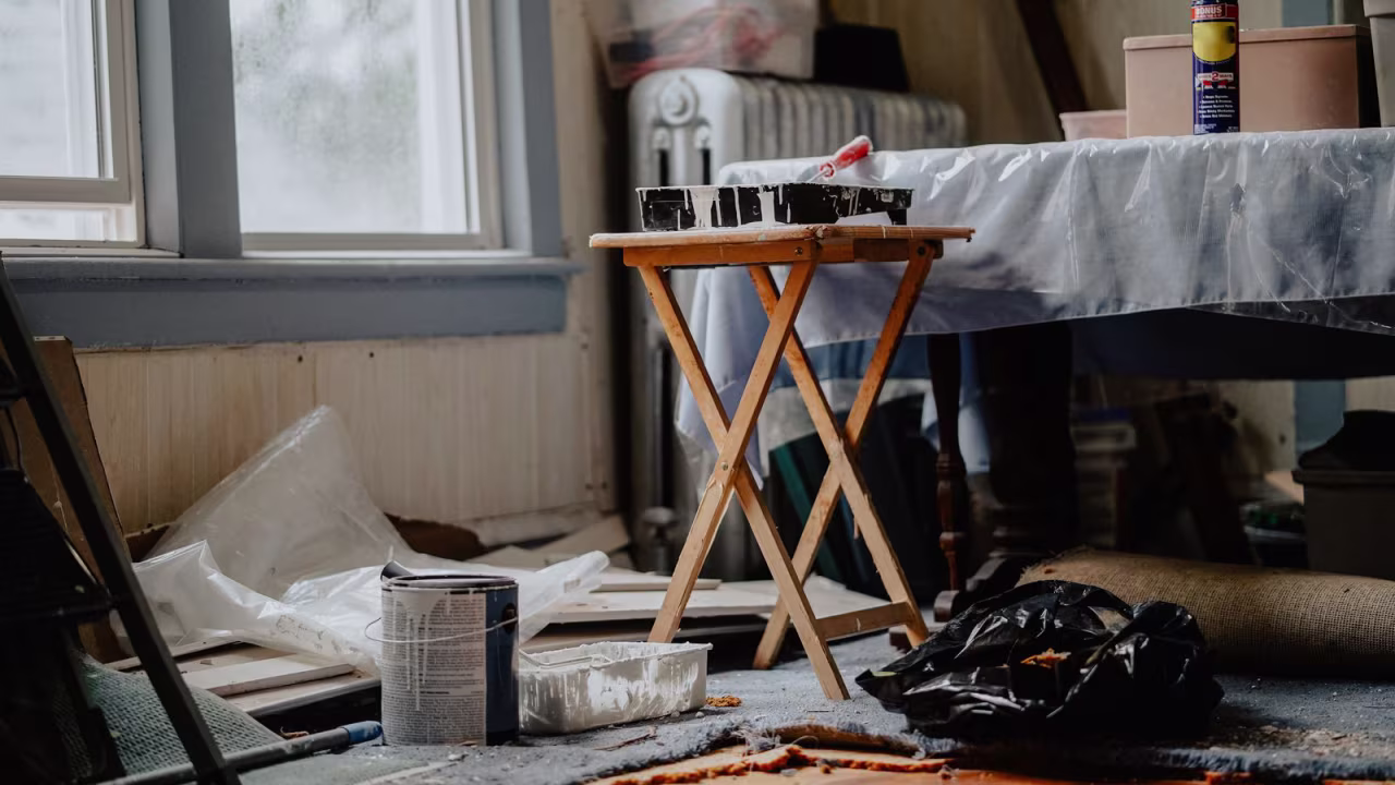 Room partway through renovation with paint supplies and a drop cloth beside a wooden table.